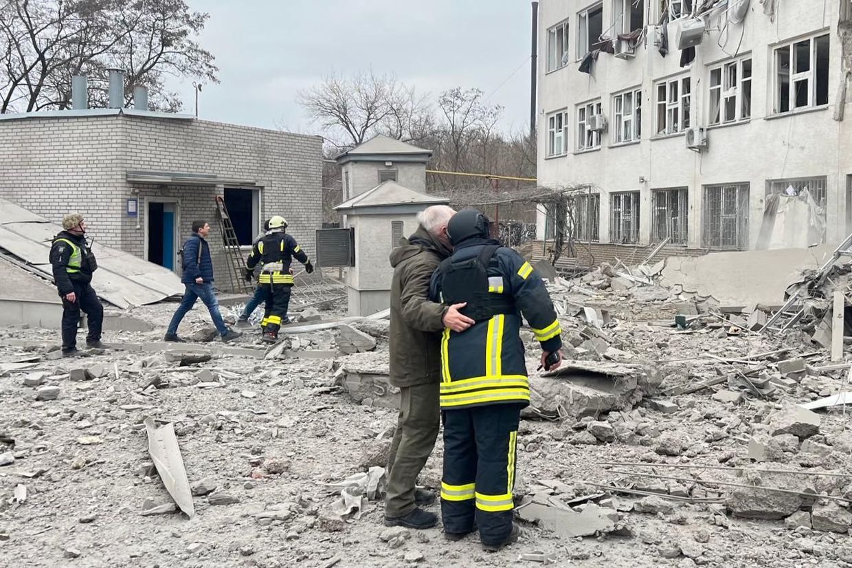 A group of firefighters hugging each other in front of a destroyed building

Description automatically generated