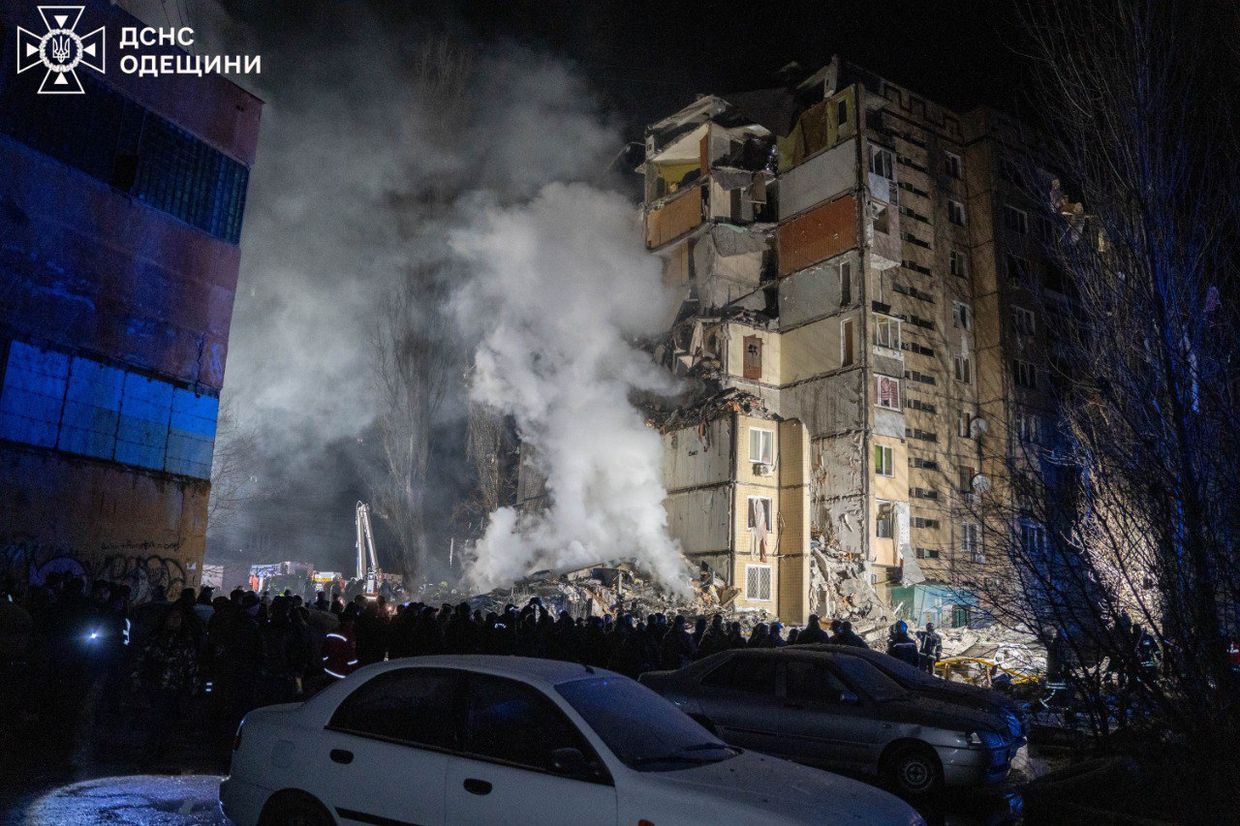 A group of people standing around a building that has a large pile of debris

Description automatically generated