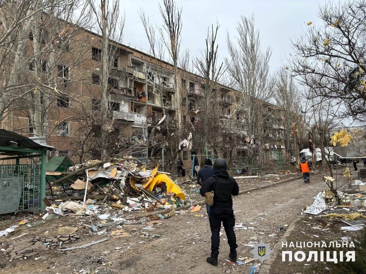 A group of people standing on a dirt road with debris in front of a building

Description automatically generated