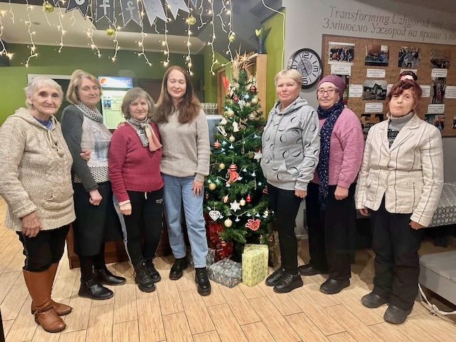 A group of women standing in front of a christmas tree

Description automatically generated