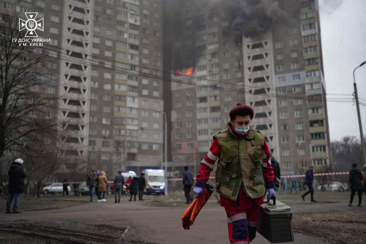 A person in a mask walking with a toolbox in front of a fire

Description automatically generated