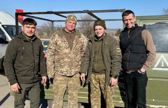 A group of men standing in front of a metal structure

Description automatically generated