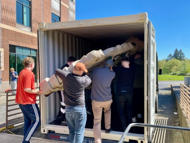 A group of people carrying a large object in a shipping container

Description automatically generated