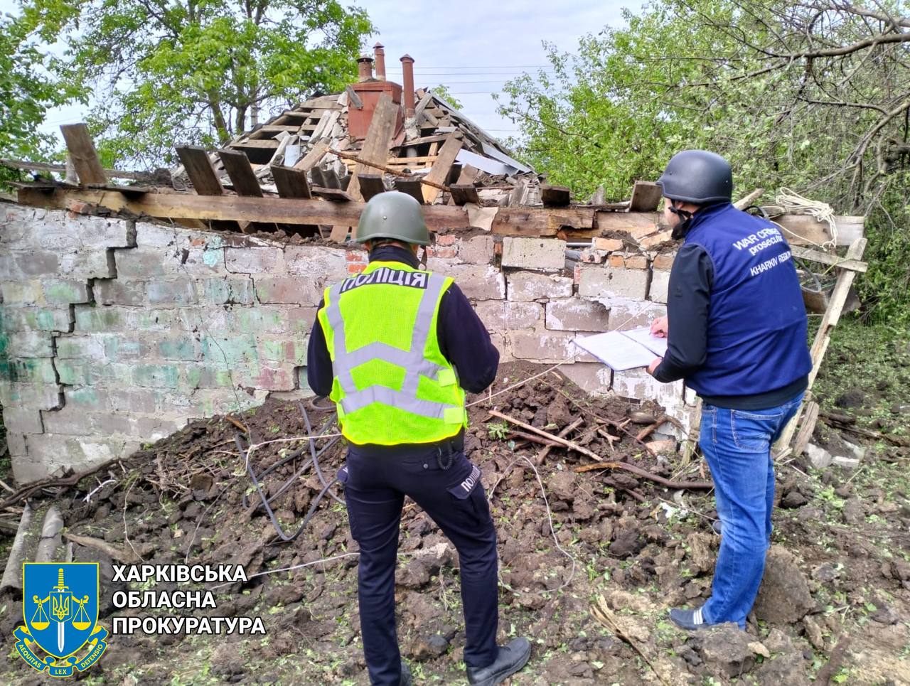 Two men in helmets standing in dirt next to a destroyed building

Description automatically generated