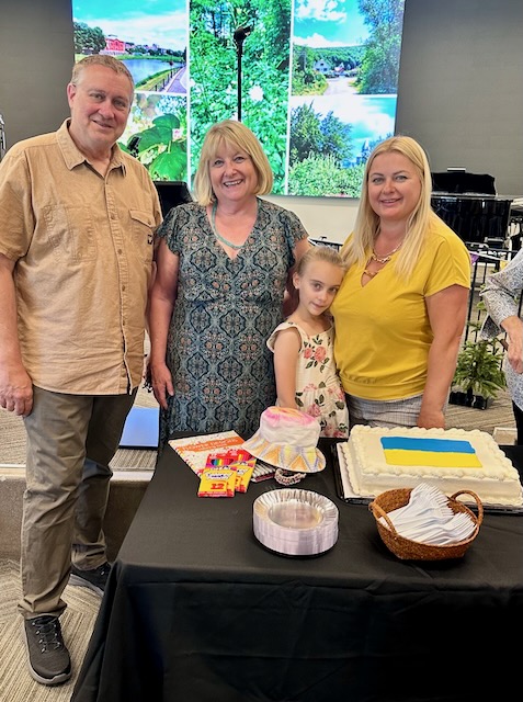 A group of people standing next to a table with a cake

Description automatically generated