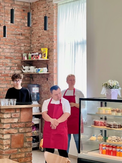 A group of people in red aprons standing in front of a glass case

Description automatically generated