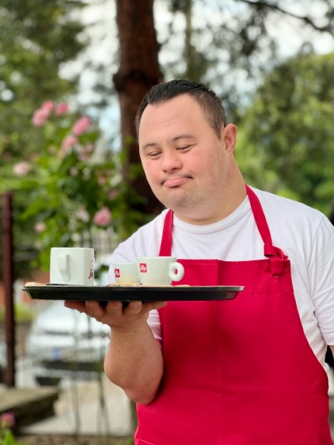 A person wearing a red apron holding a tray with two cups on it

Description automatically generated