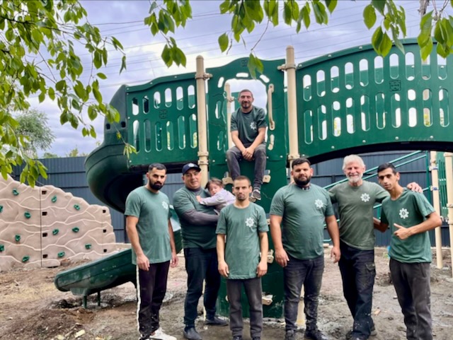 A group of men standing in front of a playground

Description automatically generated