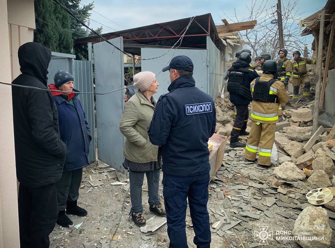 A group of people standing in front of a destroyed building

Description automatically generated