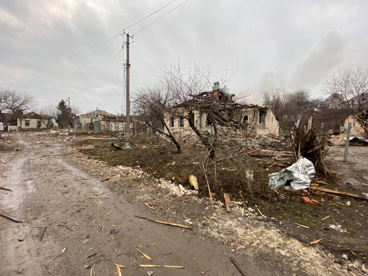 A dirt road with a destroyed house

Description automatically generated