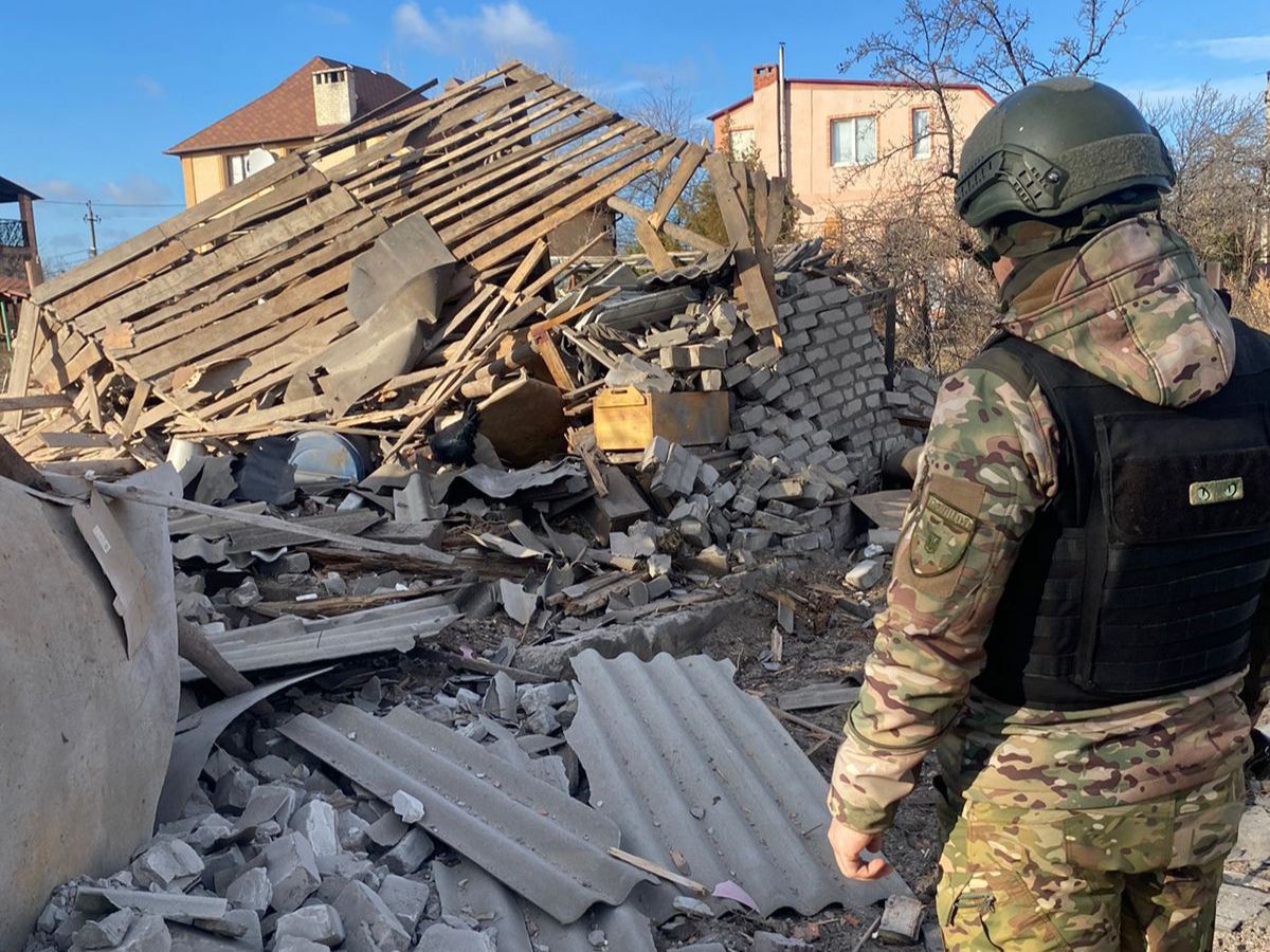 A person in military uniform walking in front of rubble

Description automatically generated