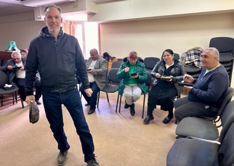 A person standing in a room with people sitting in chairs AI-generated content may be incorrect.