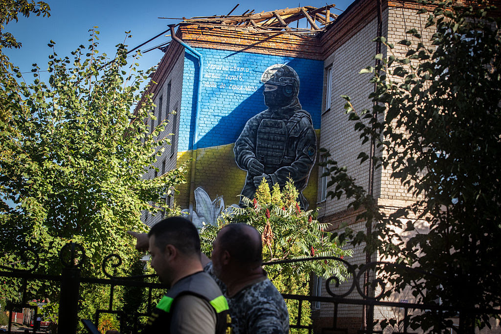 A group of people standing in front of a building with a mural on the side

AI-generated content may be incorrect.