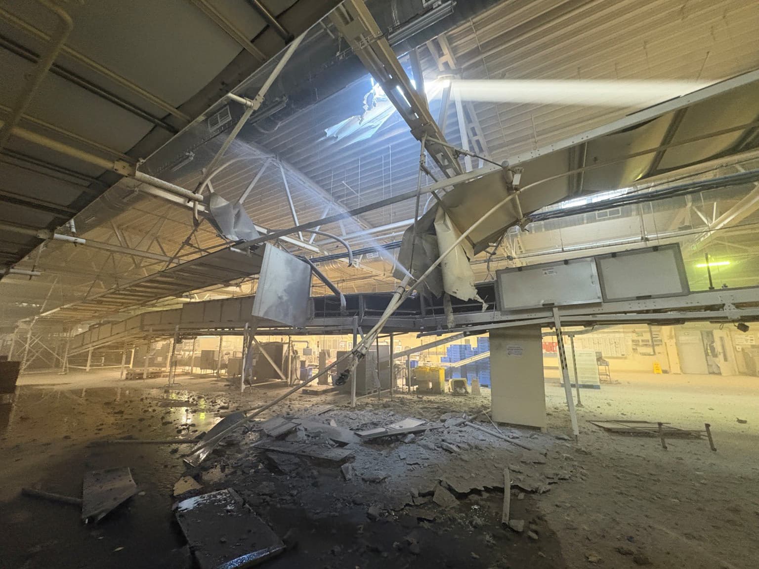 Rubble lays in a factory below a pierced hole in a metal roof