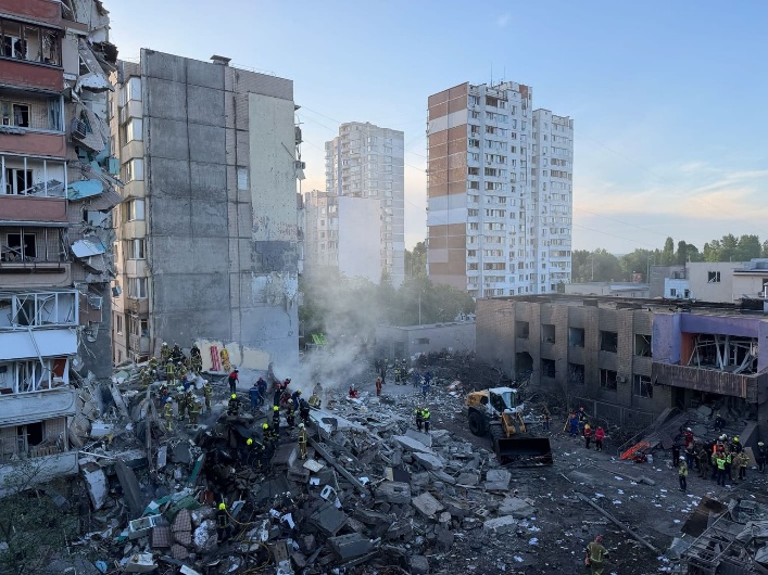 First responders stand atop a pile of rubble searching for people trapped underneath.